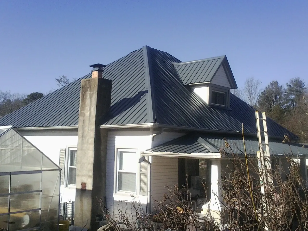 Dark blue standing seam metal roof on a white farmhouse with dormer — Slate & Tile Roof Repair by Roofing Brothers in Jewell