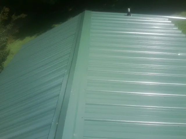 New green metal panels meeting at the ridge of a roof — Flat Roof Repair work by our crew in Jewell