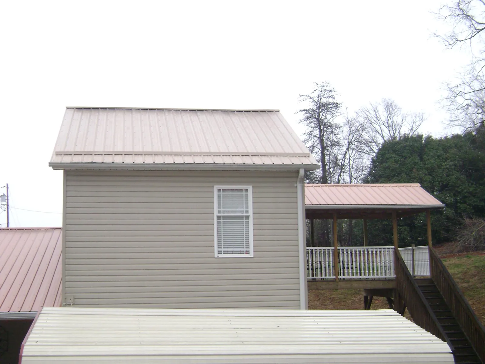 Tan metal roofs on a two story addition and attached porch, from a Roof Replacement job in Jewell
